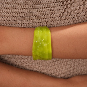 Detail view of a lime green acrylic cuff bracelet on a beige knit sweater background