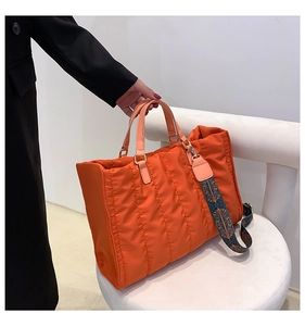 Detail of orange quilted tote bag featuring a colorful ethnic geometric fabric strap
