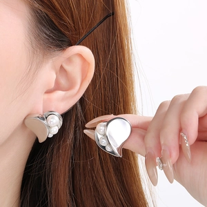 Close-up of heart-shaped silver earrings with pearl accents on model's ear