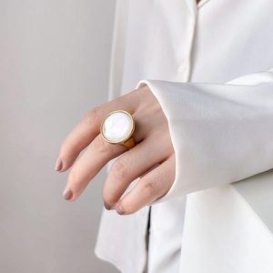 Close-up of a large round white mother of pearl ring with a golden metallic setting