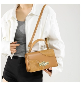 Close-up of brown PU leather handbag with crocodile pattern and wave gold metal clasp