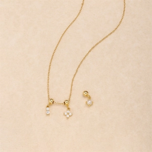Detail of clover and pearl pendants on gold chain necklace over beige texture