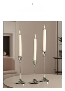 Three varying height silver candle holders with lighted white taper candles on a table