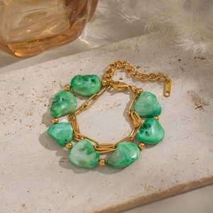 Detail of gold stainless steel bracelet with irregular green stones on a stone plate