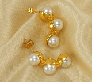 Detail of gold spiral hoop earrings with three white pearls on champagne silk fabric