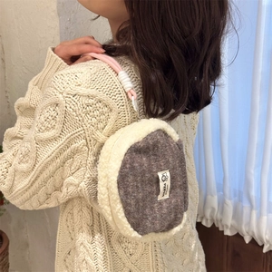 Detail of plush beige and grey shell bag with pink lanyard held by a model in a knit sweater