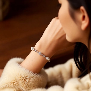 Detailed view of luxury pearl bracelet with zircon flower charm on woman's wrist