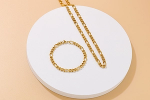 Polished gold Figaro chain necklace and bracelet set displayed on a white tray