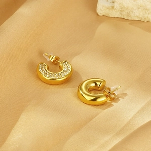 Macro shot of gold-plated C-shaped earrings with zircon inlay and butterfly backings