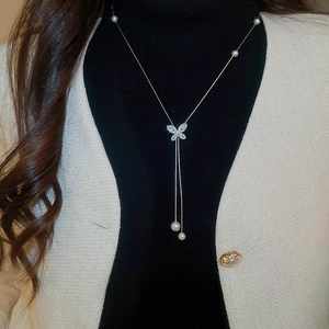 Detail of silver butterfly pendant necklace featuring white pearls and zircon tassels