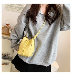 Detail of yellow woven bucket bag with drawstring closure and slim crossbody strap