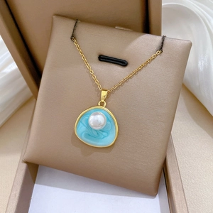 Détail d'un collier doré avec pendentif ovale en émail bleu clair et perle blanche