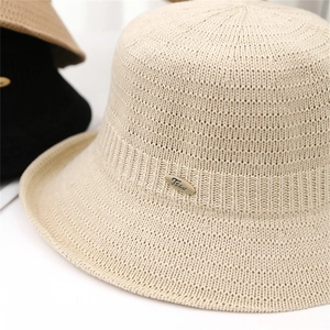 Detailed close-up of knit texture and oval metal logo on a beige crochet bucket hat