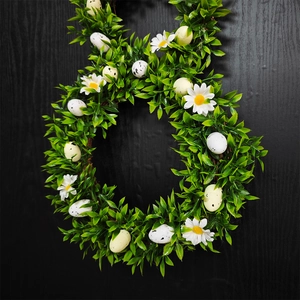 Easter bunny wreath with green leaves, daisies and speckled eggs on black wood