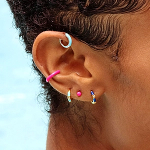 Macro shot of colorful enamel hoop earrings and cubic zirconia studs set on ear