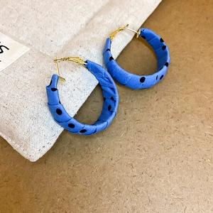 Close-up of klein blue fabric wrapped hoop earrings with black polka dots and gold hooks