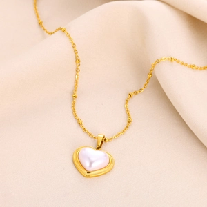 Detail of gold heart pendant with white pearl inlay on soft beige fabric background