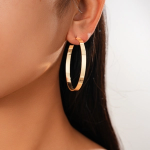 Close-up of model wearing large flat-edged golden geometric hoop earrings in a minimalist style