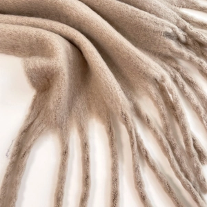 Close-up of soft mohair texture and twisted fringe detail of a camel winter scarf