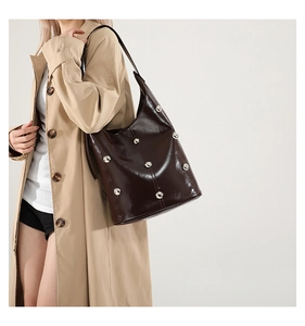 Detail of dark brown patent leather shoulder bag with silver rivet studs and glossy finish