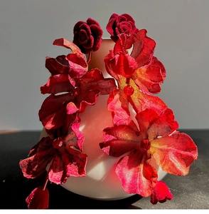 Detailed view of red fabric rose flower earrings displayed on a white ceramic vase