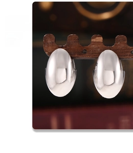 Close-up of oval silver titanium steel earrings hanging on a premium wooden stand