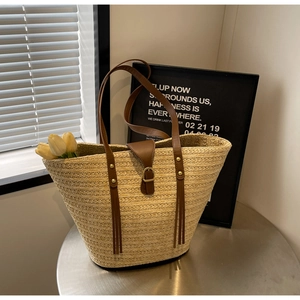Detail of straw tote bag with brown PU leather straps and metal buckle on metal table