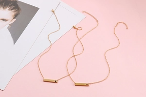 Macro detail of two gold horizontal bar necklaces with small heart and zircon inlay