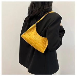 Close-up of a bright yellow crocodile pattern underarm bag worn by a model