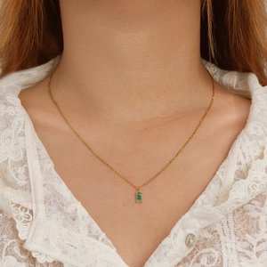 Close-up of a gold necklace featuring a rectangular green zircon pendant on white lace