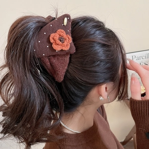 Detail view of a plush flower triangle hair claw with knitted orange blossom decor