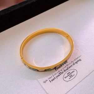 Vue détaillée d'un bracelet doré émaillé aux motifs floraux sur fond beige texturé