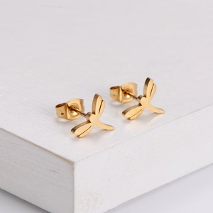 Macro shot of minimalist golden dragonfly stud earrings on white textured podium