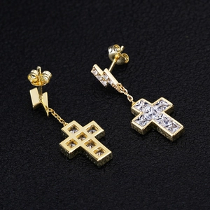 Nahaufnahme goldener Kreuz- und Blitzohrringe mit Zirkon auf schwarzem Lederhintergrund