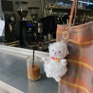 Close-up of a white plush sheep keychain with a red collar on a checkered tote bag