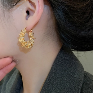 Détail de boucles d'oreilles torsadées dorées avec zircons portées par un mannequin