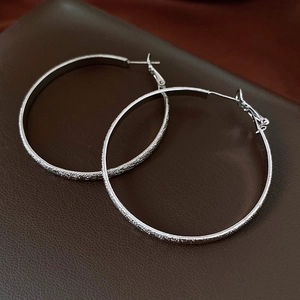 Gros plan sur les boucles d'oreilles argentées en C avec texture givrée sur cuir sombre