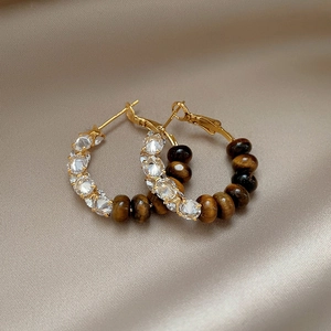 Elegant gold earrings with tiger eye stones and zircons on champagne silk background