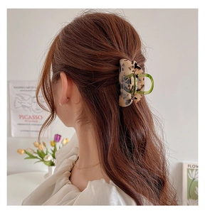 Green resin hair claw clip with tortoise pattern on a model in a cozy setting