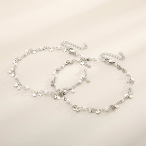 Silver star and sequin charm anklets with white pearls on a soft beige background