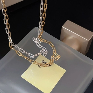 Detailed view of polished gold and silver paperclip chain necklaces on a glass bottle