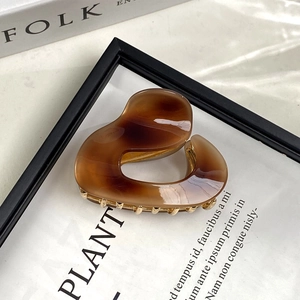 Detail of amber acetate heart hair claw clip styled on a black frame and book background