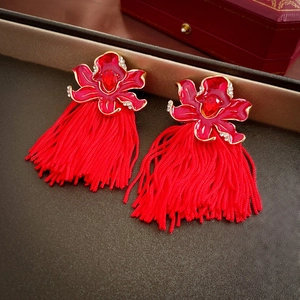 Detailed close-up of red floral earrings with golden edges and long silk tassels