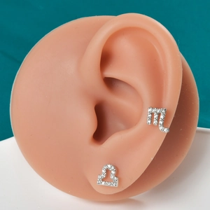 Detail of Scorpio and Libra zodiac ear studs with tiny cubic zirconia on a model ear