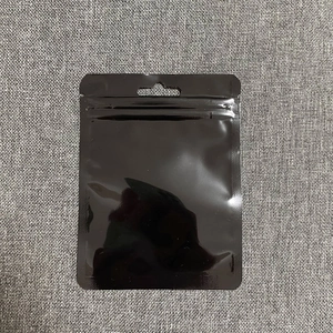 Black plastic self-sealing pouch with hanging hole and zipper on gray fabric