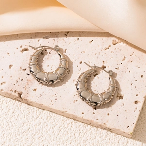 Macro detail of silver bamboo-textured C-shape earrings on a premium silk and stone backdrop