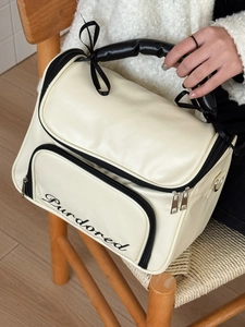 Ballet style cream leather cosmetic bag with black bow and embroidery on a wooden chair