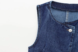 Dettaglio del gilet in denim blu scuro con cuciture a contrasto e bottone in metallo