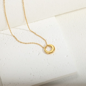 Detail view of a 14K gold plated minimalist circular pendant on a textured stone base