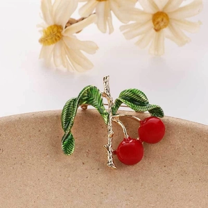 Detail of a cherry enamel brooch with green leaves on a beige ceramic tray